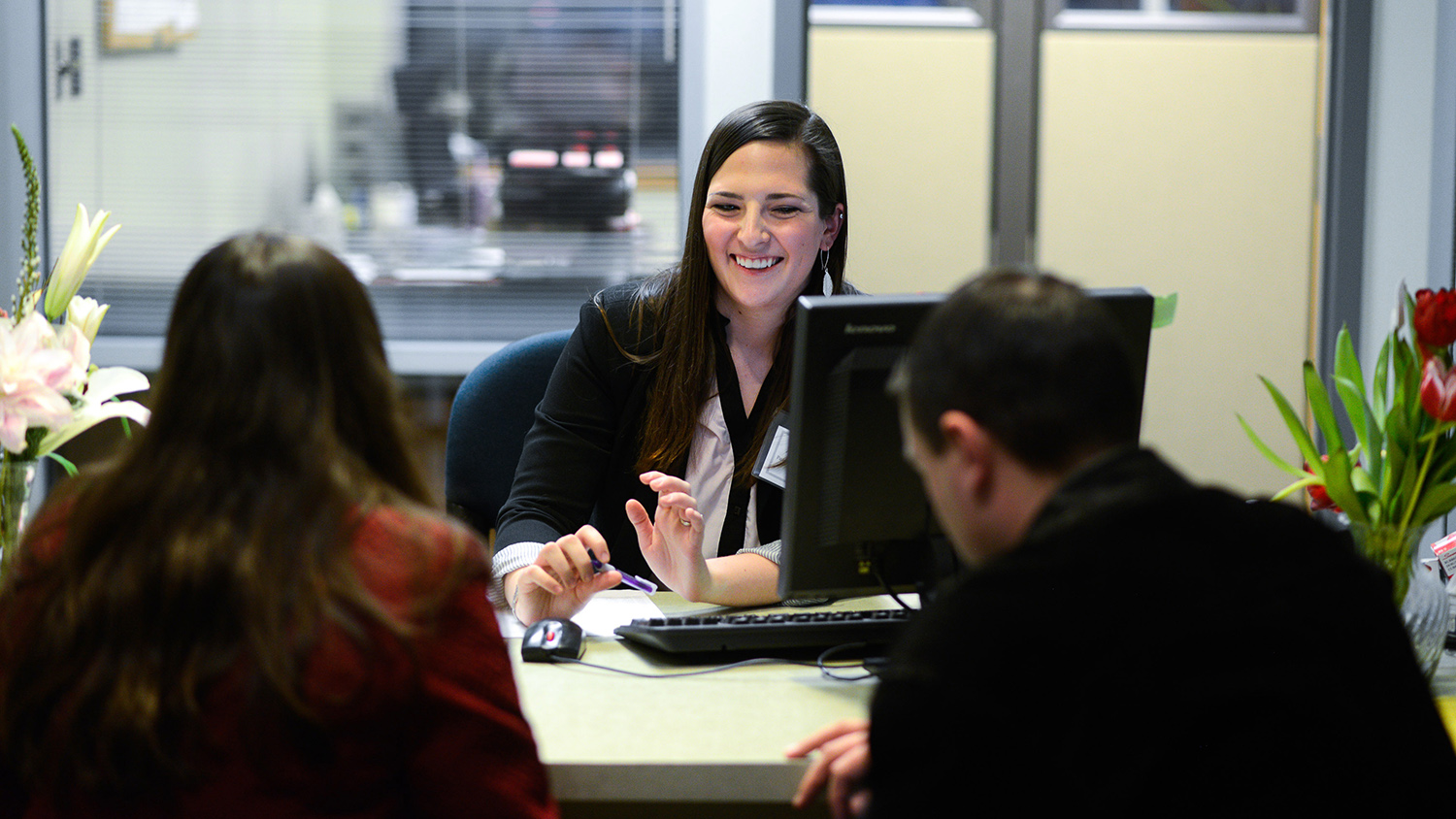 A student sits behind a desk and talks to two people