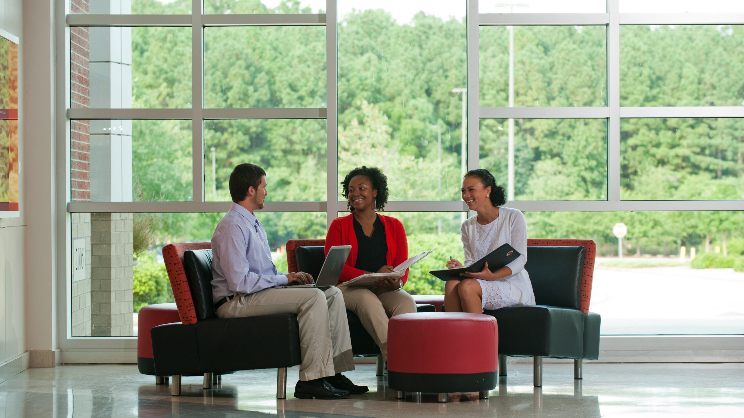 Photo of three people sitting and discussing in the lobby of a building